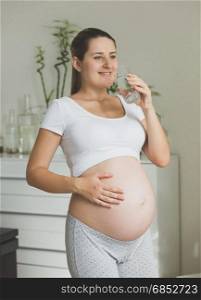 Portrait of happy pregnant woman posing with glass of water at morning