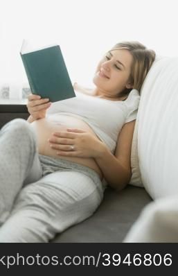 Portrait of happy pregnant woman reading book on sofa