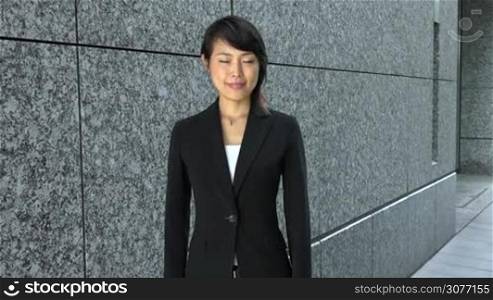 Portrait of happy pretty Japanese female manager looking at camera. Young Asian businesswoman, confident girl, elegant woman smiling near office building. Career, success. Slow motion