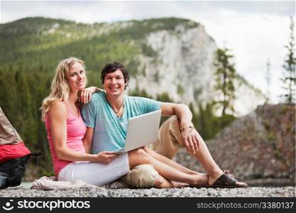 Portrait of happy relaxed young couple with laptop while camping