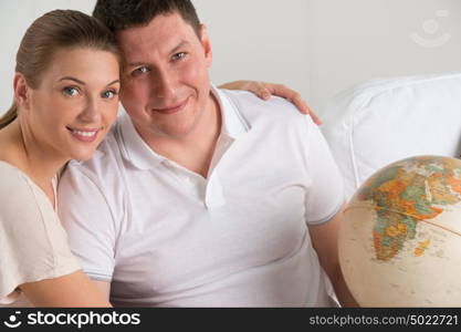 Portrait of happy romantic couple sitting together at home with globe planning their vacation and trip. Travelling concept