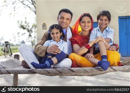 Portrait of happy rural Indian family sitting on cot