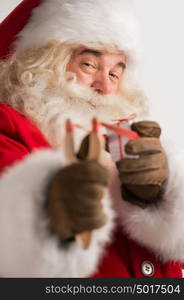 Portrait of happy Santa Claus aiming christmas gift with slingshot and looking at camera