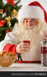 Portrait of happy Santa Claus at home looking at camera while eating cookies and drinking tea
