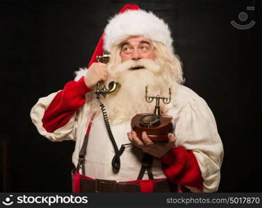 Portrait of happy Santa Claus calling phone against dark background