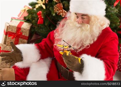 Portrait of happy Santa Claus holding gift helicopter toy in his hands sitting near Christmas tree