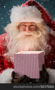 Portrait of happy Santa Claus opening gift box outdoors at North Pole. Magical light from box on his face