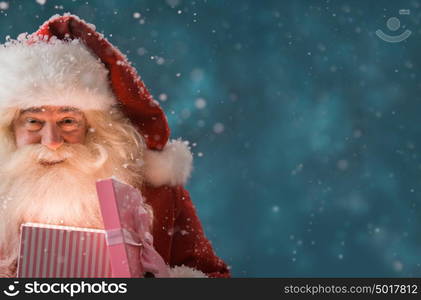 Portrait of happy Santa Claus opening gift box outdoors at North Pole. Magical light from box on his face