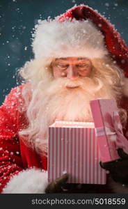 Portrait of happy Santa Claus opening gift box outdoors at North Pole. Magical light from box on his face