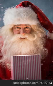 Portrait of happy Santa Claus opening gift box outdoors at North Pole. Magical light from box on his face