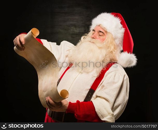 Portrait of happy Santa Claus reading Christmas letter against dark background