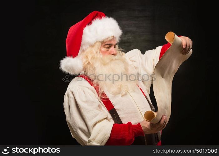 Portrait of happy Santa Claus reading Christmas letter against dark background