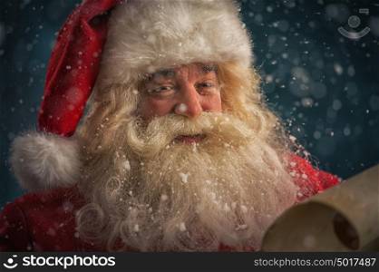 Portrait of happy Santa Claus reading Christmas letter outdoors at north pole under snowfall