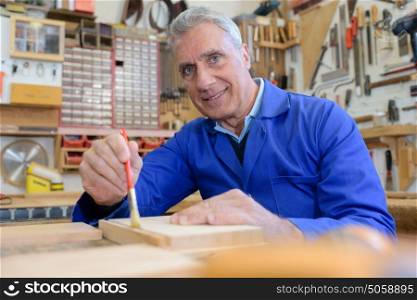 portrait of happy senior carpenter varnishing wood in workshop