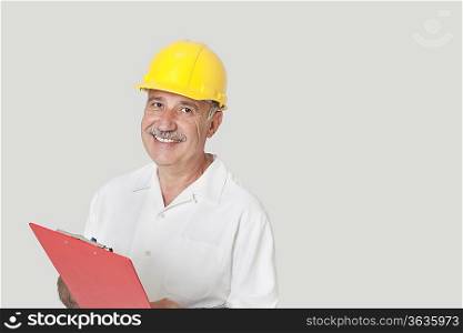 Portrait of happy senior constructor with clipboard over gray background