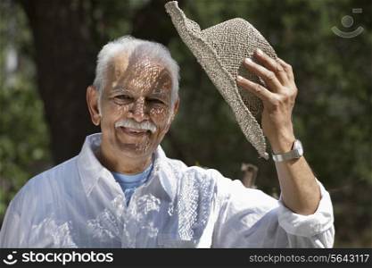 Portrait of happy senior man holding hat while smiling at park