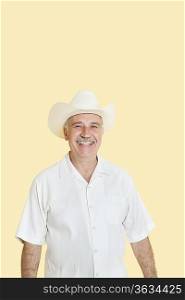 Portrait of happy senior man wearing cowboy hat over yellow background