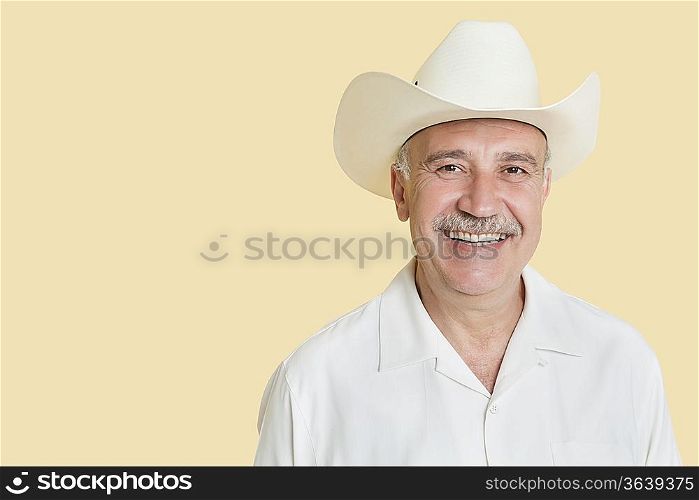 Portrait of happy senior man wearing cowboy hat over yellow background
