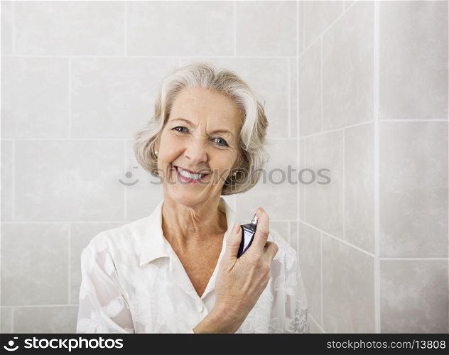Portrait of happy senior woman spraying perfume in bathroom