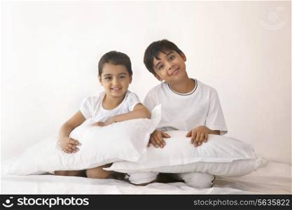 Portrait of happy siblings with pillows sitting in bed