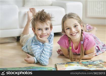 Portrait of happy siblings with story books lying on floor in living room