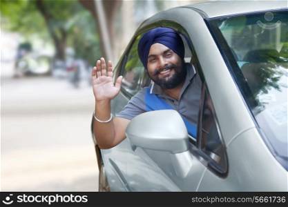 Portrait of happy Sikh man waving out of car window