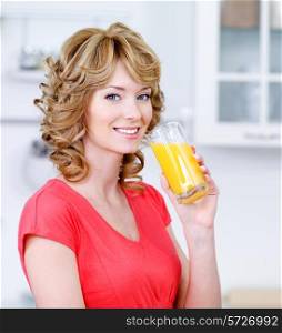 Portrait of happy smiling blonde woman drinking fresh orange juice in the kitchen
