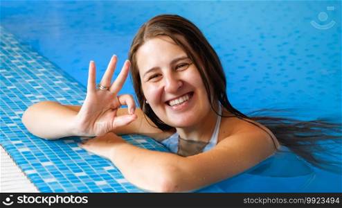 Portrait of happy smiling brunette woman relaxing in swimming pool and showing OK sign with fingers. Portrait of happy smiling brunette woman relaxing in swimming pool and showing OK sign with fingers.