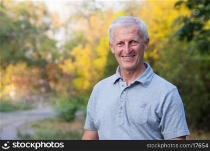 portrait of happy smiling face of grey-haired old man. Outdoor. Blue jeans. Grey t-shirt.