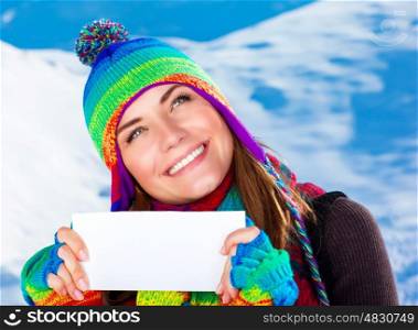 Portrait of happy smiling girl holding in hands blank greeting card on snowy mountains background, text space for congratulations with Christmas holidays