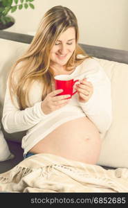 Portrait of happy smiling pregnant woman sitting on sofa with cup of tea