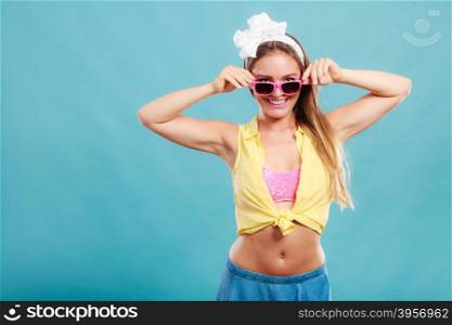 Portrait of happy smiling pretty pin up girl with hairband bow wearing sunglasses. Attractive gorgeous young retro woman posing in studio on blue background.
