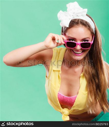 Portrait of happy smiling pretty pin up girl with hairband bow wearing sunglasses. Attractive gorgeous young retro woman posing in studio on green background.