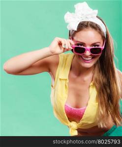 Portrait of happy smiling pretty pin up girl with hairband bow wearing sunglasses. Attractive gorgeous young retro woman posing in studio on green background.