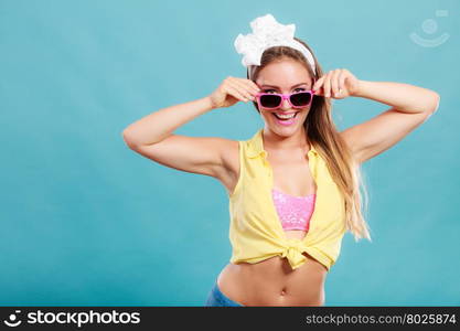 Portrait of happy smiling pretty pin up girl with hairband bow wearing sunglasses. Attractive gorgeous young retro woman posing in studio on blue background.