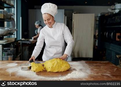 Portrait of happy smiling woman baker cut piece of dough with knife on wooden table sprinkled with flour. Step-by-step recipe for cooking pastry concept. Happy smiling woman baker cut piece of dough with knife on wooden table