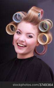 Portrait of happy smiling woman in beauty salon. Blond girl with hair curlers rollers by hairdresser. Hairstyle.