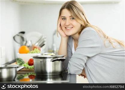 Portrait of happy smiling woman posing on kitchen and cooking soup