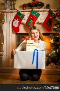 Portrait of happy smiling woman posing with present boxes at fireplace