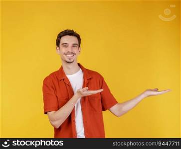 Portrait of happy smiling young man presenting and showing your text or product isolated on yellow background. Empty copyspace area for slogan or advertising text message.