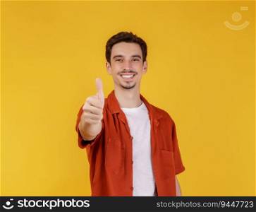 Portrait of happy smiling young man showing thumbs up gesture and looking at camera on isolated over yellow background. Success concept.