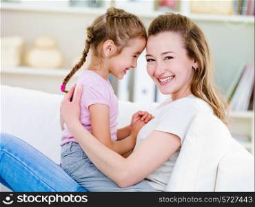 Portrait of happy smiling young woman with her little pretty daughter - indoors