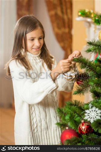 Portrait of happy teenage girl in woolen sweater decorating Christmas tree at house