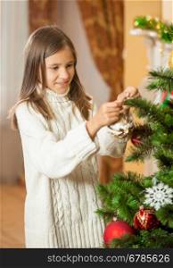 Portrait of happy teenage girl in woolen sweater decorating Christmas tree at house