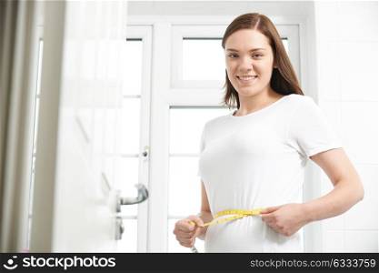 Portrait Of Happy Teenage Girl Measuring Waist In Bathroom