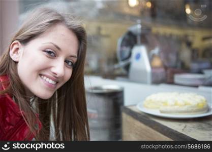 Portrait of happy woman by display cabinet in cafe