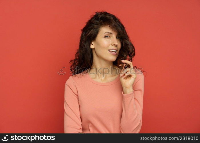 Portrait of happy woman enjoy healthy natural hair. Curly brunette female touch beautiful brown curls satisfied after beauty hairstyle treatment isolated over red background. Wellness and care concept. Happy woman play with healthy natural hair. Curly brunette female touch brown curls after treatment