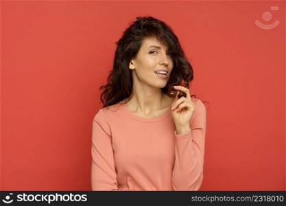 Portrait of happy woman enjoy healthy natural hair. Curly brunette female touch beautiful brown curls satisfied after beauty hairstyle treatment isolated over red background. Wellness and care concept. Happy woman play with healthy natural hair. Curly brunette female touch brown curls after treatment