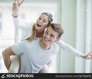 Portrait of happy woman enjoying piggyback ride given by man at home
