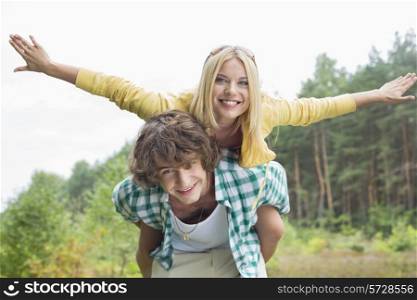 Portrait of happy woman enjoying piggyback ride on man in forest